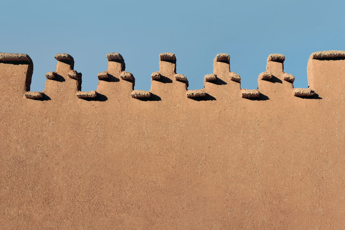 Traditional Moroccan earthen wall with repeating architectural details against a clear blue sky, symbolizing rhythm, beauty, and meaningful travel.