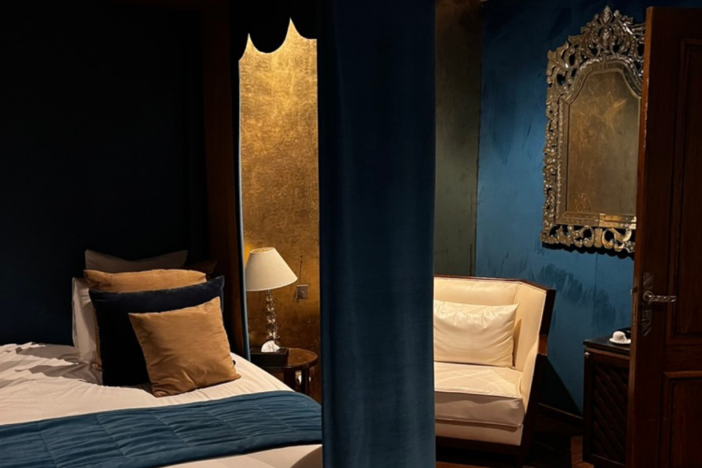 Blue and gold hotel room with bed, armchair and decorative mirror