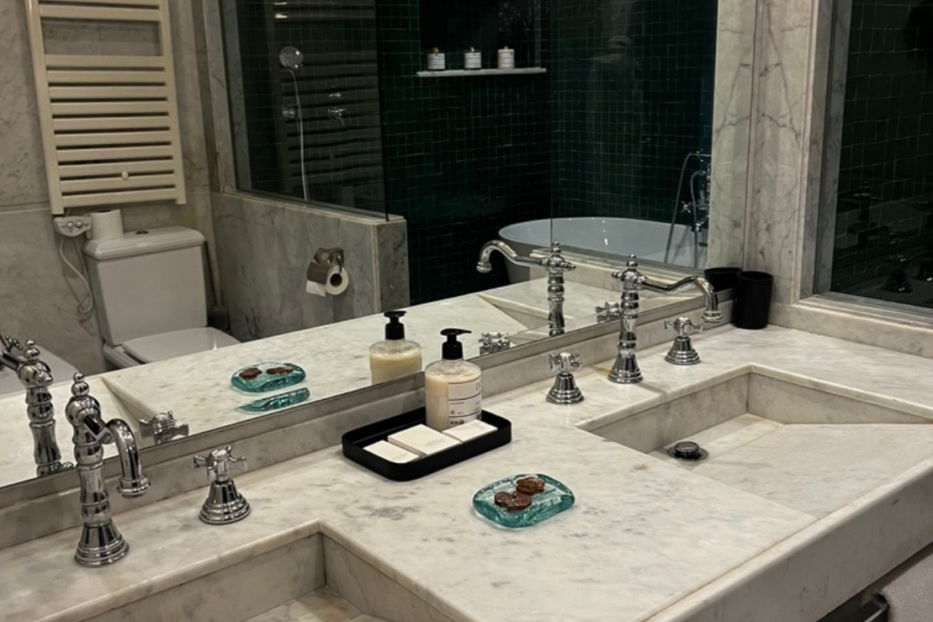 Marble hotel bathroom with double sinks, bathtub and dark green tiles