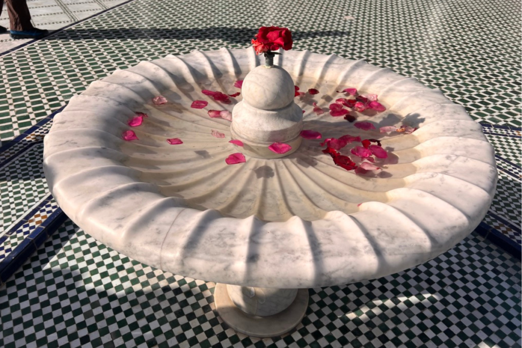 White marble fountain with rose petals surrounded by green Moroccan tiles