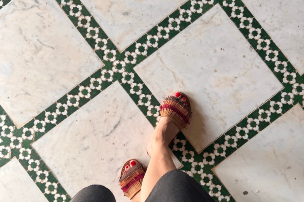Woman wearing sandals standing on marble and green zellige tiles in Morocco
